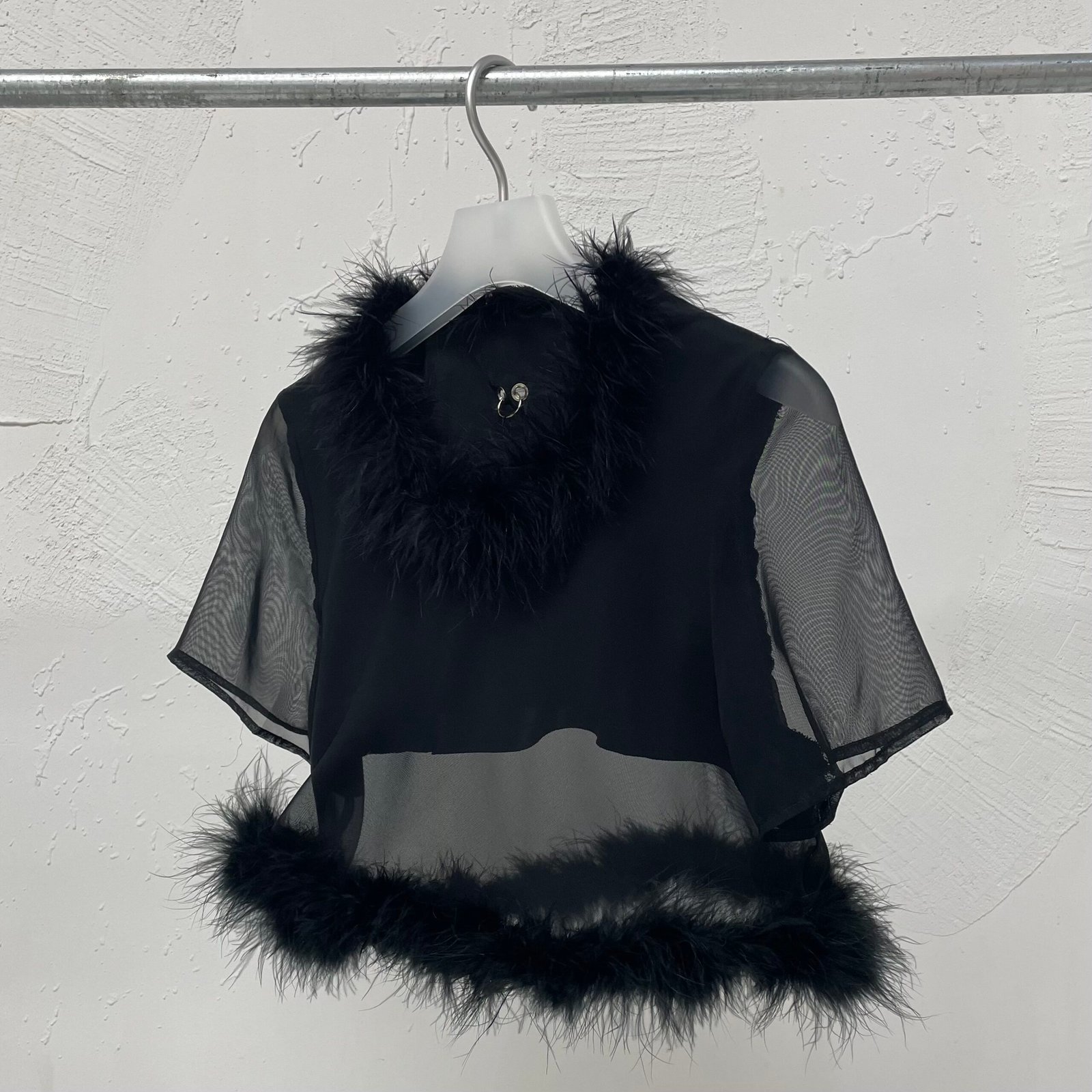 Camiseta corta negra upcycling con diseño translúcido en capas, detalles de plumas en cuello y borde inferior, y piercing decorativo en la espalda.