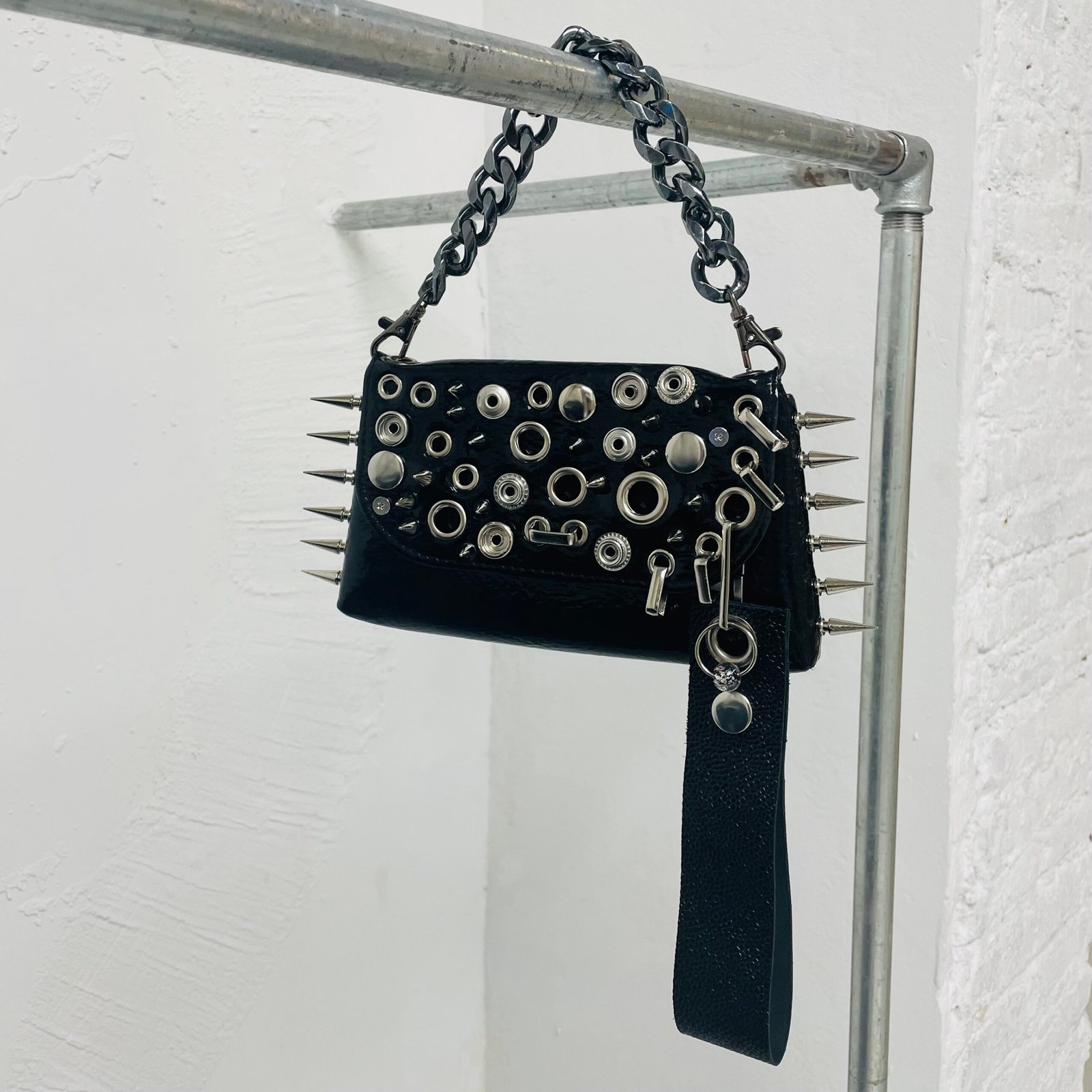 Mini bolso negro acharolado con acabado brillante, detalles punk de tachas, piercings y pinchos metálicos. Incluye llavero. Pieza única.